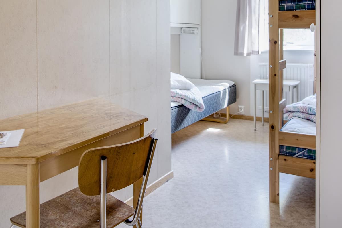 Ein Zimmer mit einem Holztisch, einem Stuhl, einem Etagenbett und einem Deckenventilator.