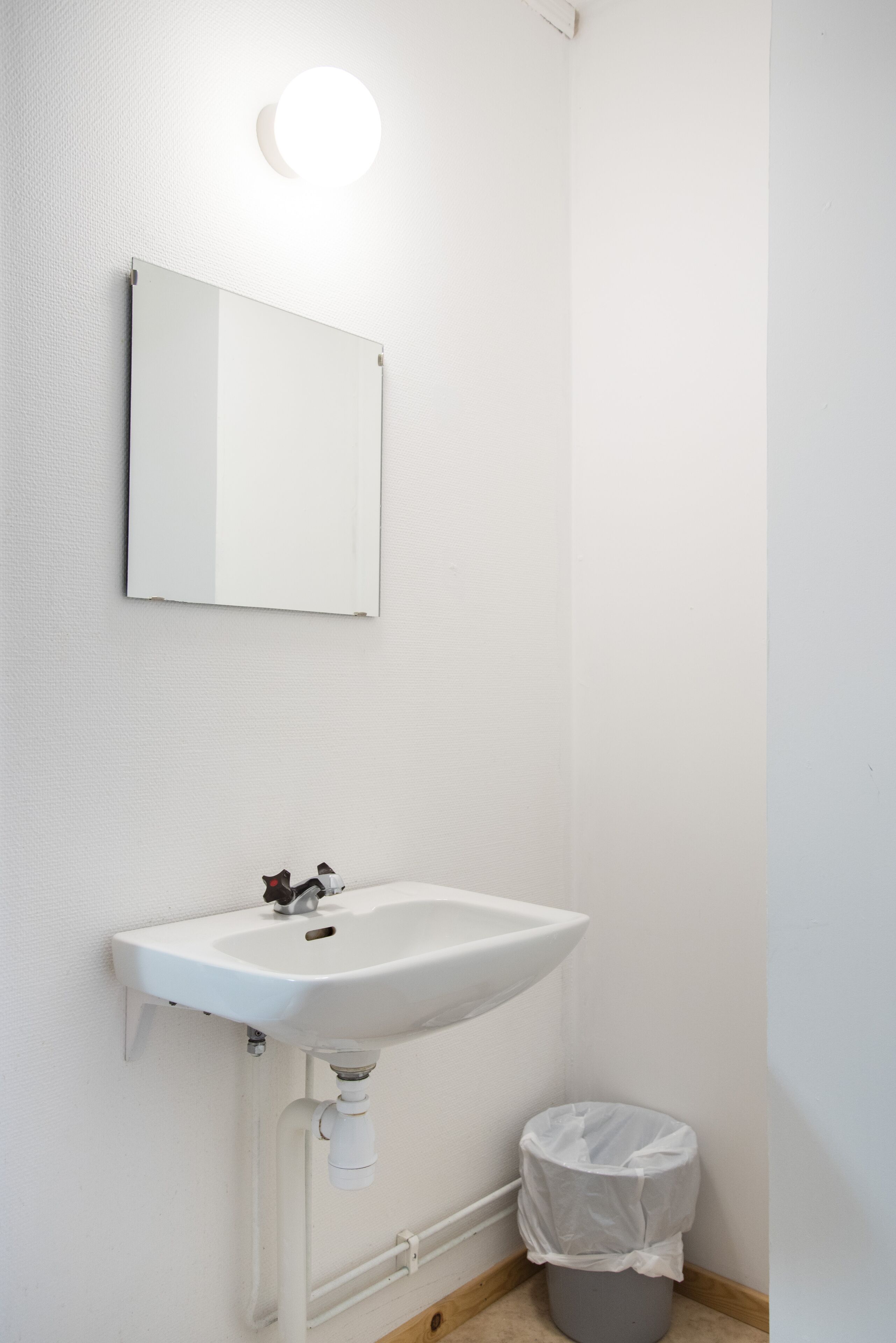 A bathroom with a white sink, a mirror, and a round light fixture.