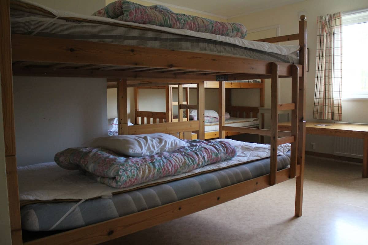 Ein Schlafzimmer mit Etagenbetten, einem Holzkopfende, einem Schreibtisch und einem Fenster mit Vorhängen.