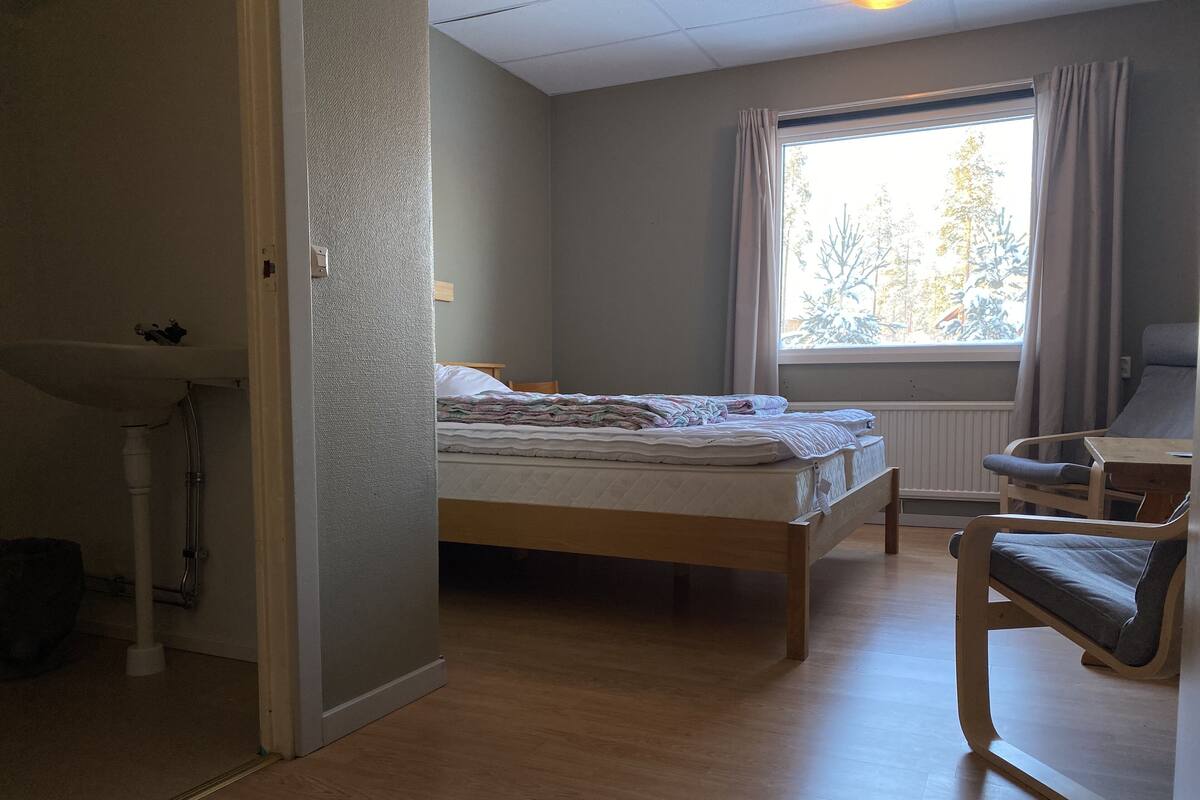 Ein Schlafzimmer mit Bett, Sessel, Fenster mit Vorhängen und Heizkörper.