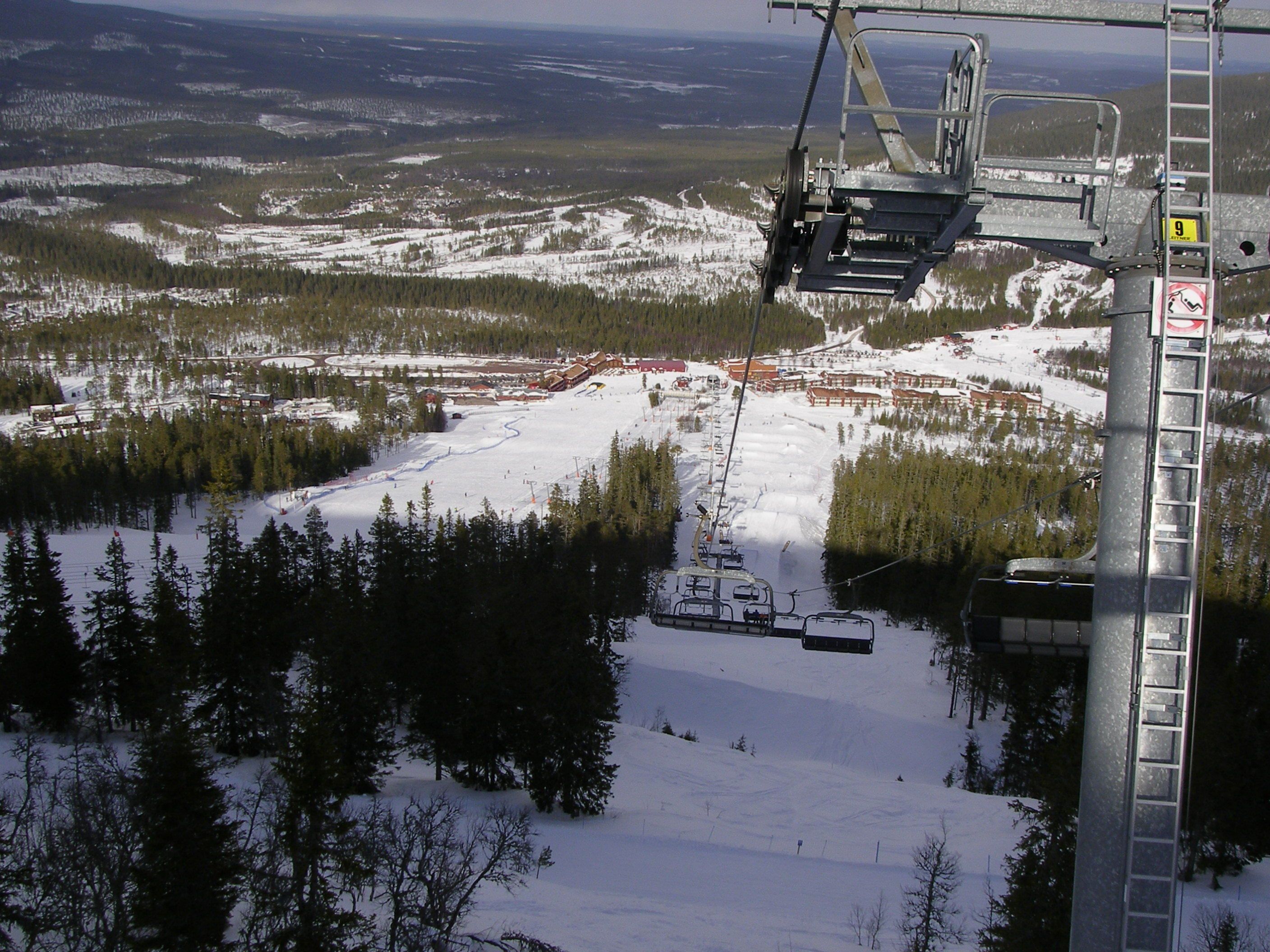 A ski lift chair suspended over a snowy landscape with a view of a ski resort below.