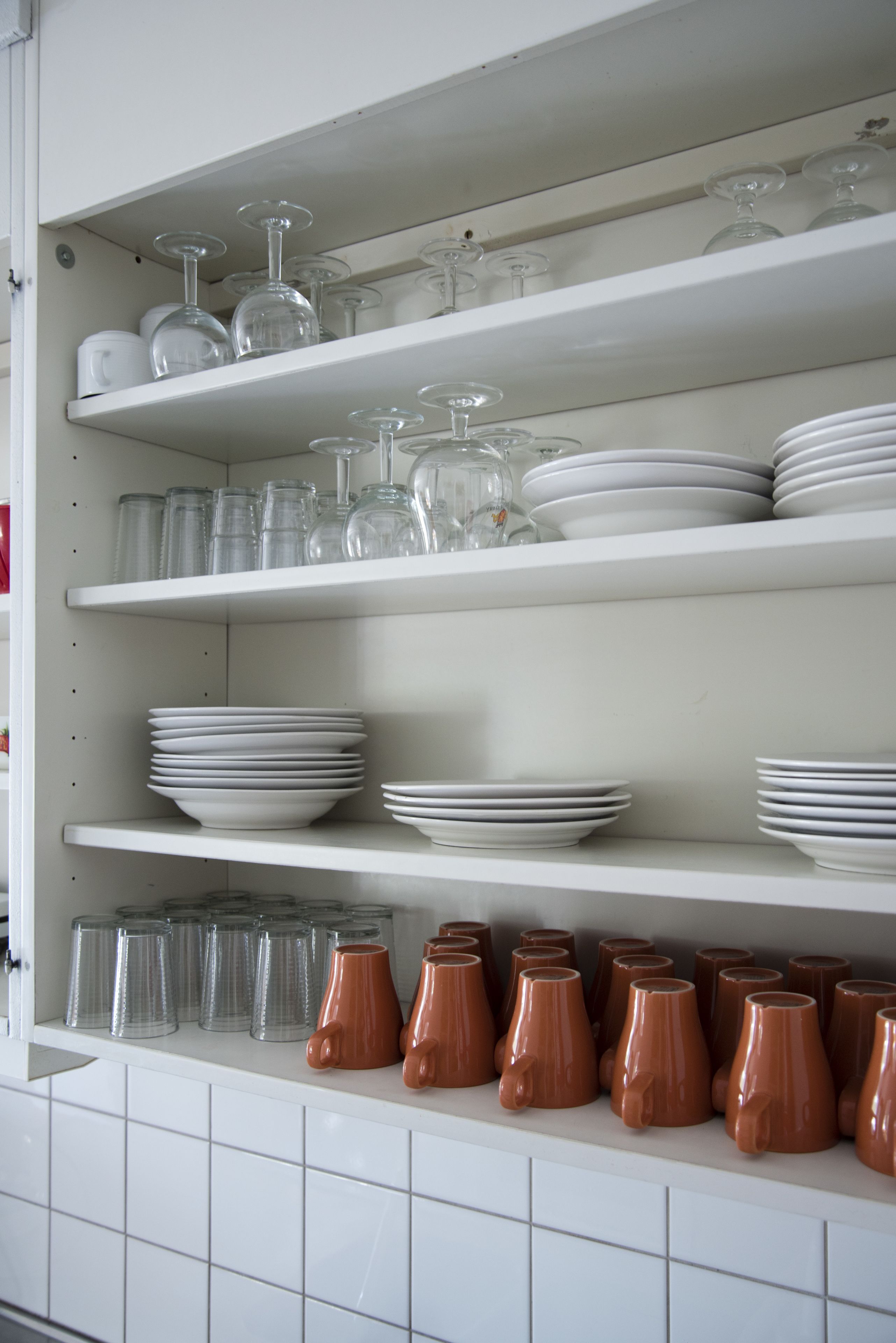 Una cocina con estantes blancos que contienen platos, vasos y tazas.