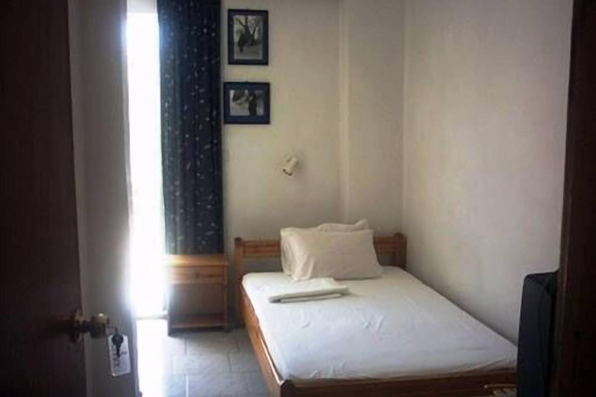 A small, single-bed room with a wooden headboard, a white bedspread, and two framed pictures on the wall.