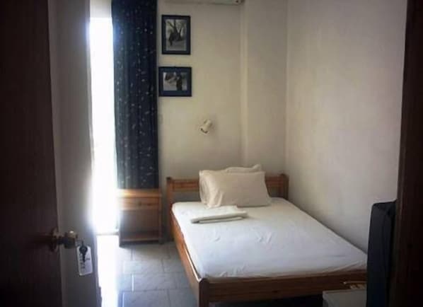 Una habitación pequeña con cama individual, cabecera de madera, colcha blanca y dos cuadros en la pared.