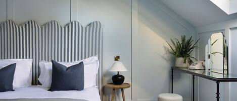 A neatly arranged bedroom with a bed, bedside table, lamp, and a small stool.