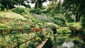 Un jardín con fuente de agua, cerca de madera y diversas plantas y flores.