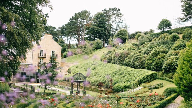Un jardín con un pabellón, un edificio con balcón y una variedad de plantas y flores.