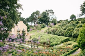A garden with a gazebo, a building with a balcony, and a variety of plants and flowers.