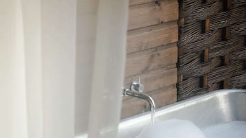 Un baño con un lavamanos de acero inoxidable, una pared de madera y una cesta tejida.