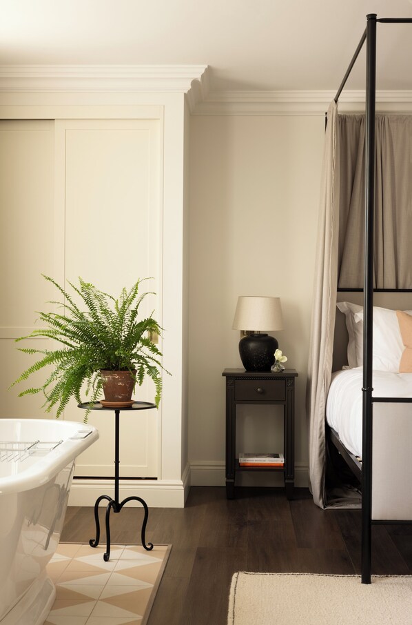 A bedroom with a four-poster bed, a bedside table with a lamp, a potted plant, and a small bedside table with a book. - Saltmoore (Whitby)