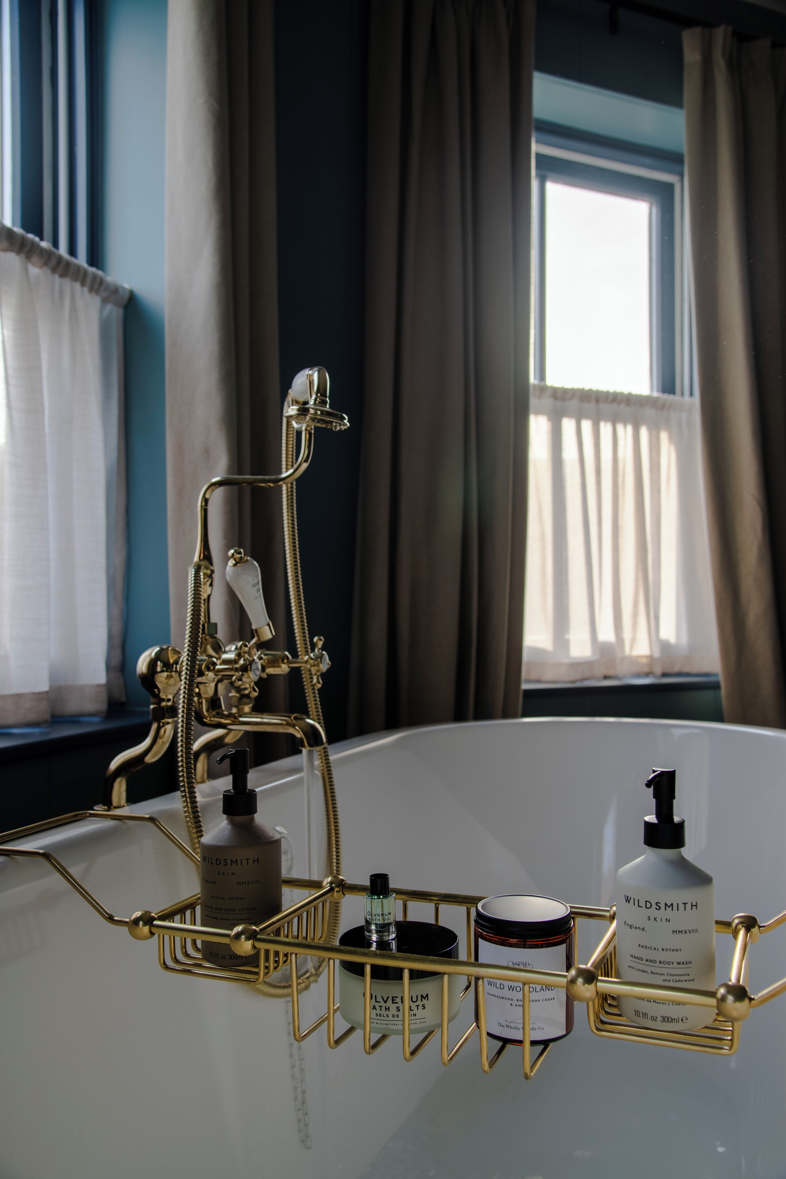 Een badkamer met een gouden wastafelmeubel, een douche en een raam met gordijnen.