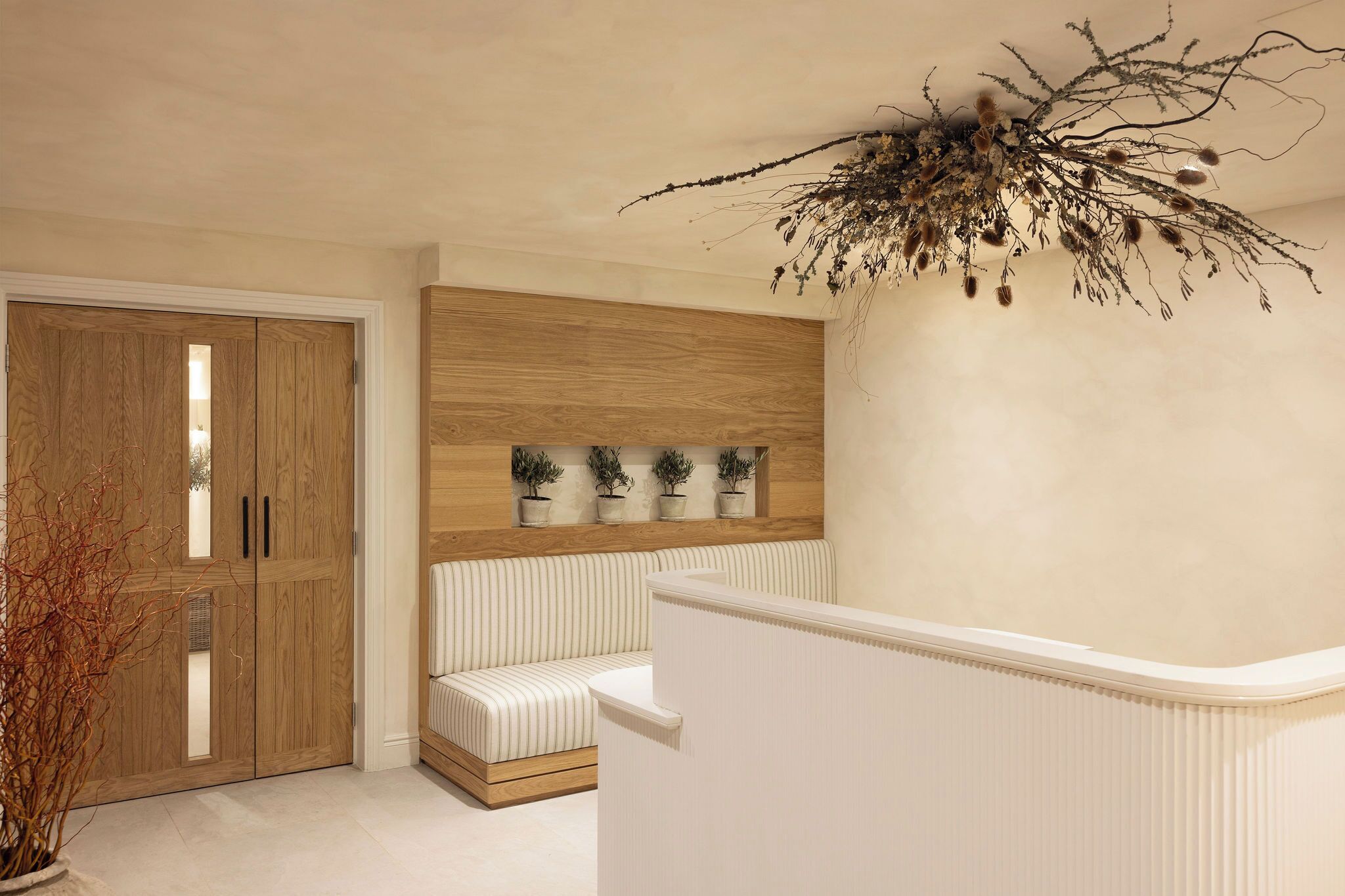 A room with a wooden wardrobe, a bench, a wall-mounted shelf with potted plants, and a ceiling decoration.