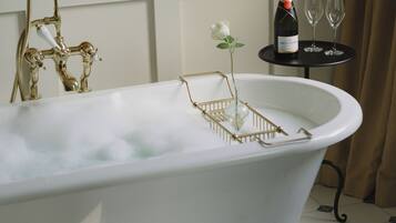 A bathtub with a gold faucet, a bottle of champagne, and two glasses on a small table beside it.