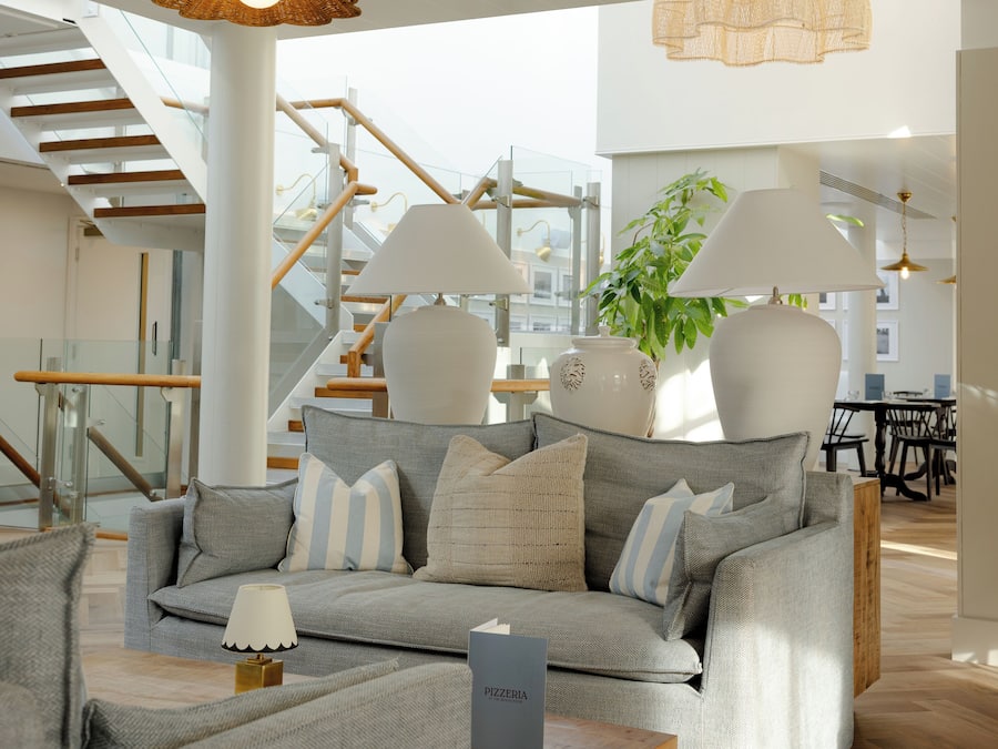 Ein modernes Wohnzimmer mit einem grauen Sofa, zwei weißen Lampen und einem Holztisch.
