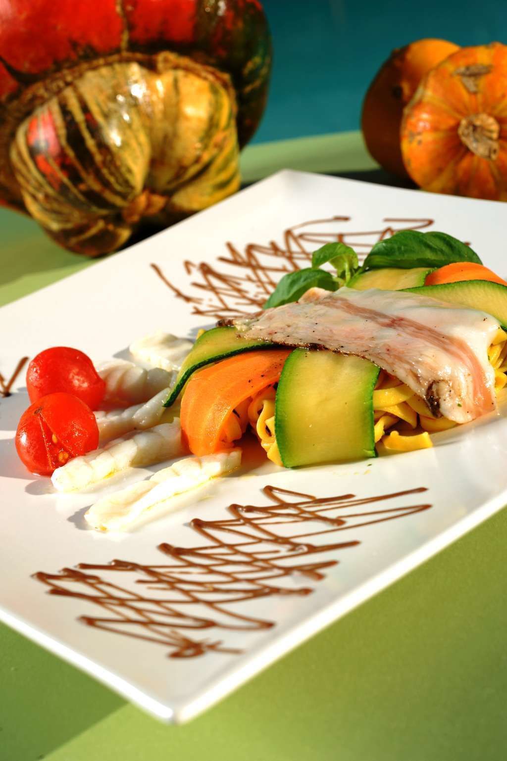 Un plato cuadrado con ensalada, que incluye vegetales cortados y un trozo de carne, decorado con un chorrito de chocolate.