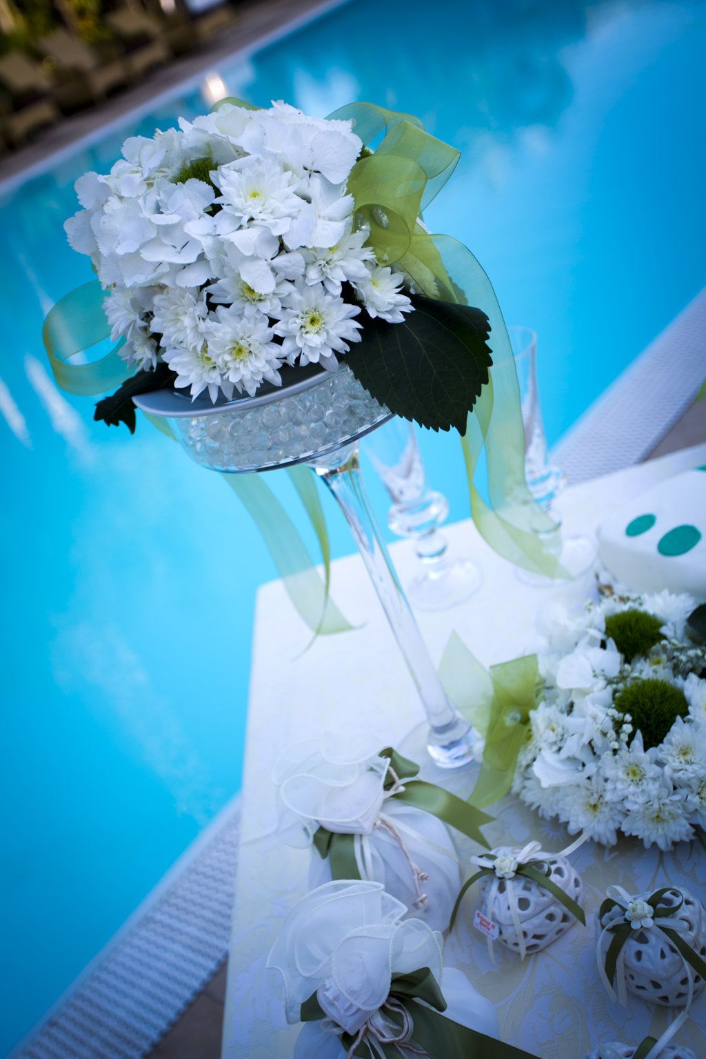 A table with a glass vase containing white flowers, a glass candle holder, and small decorative items.