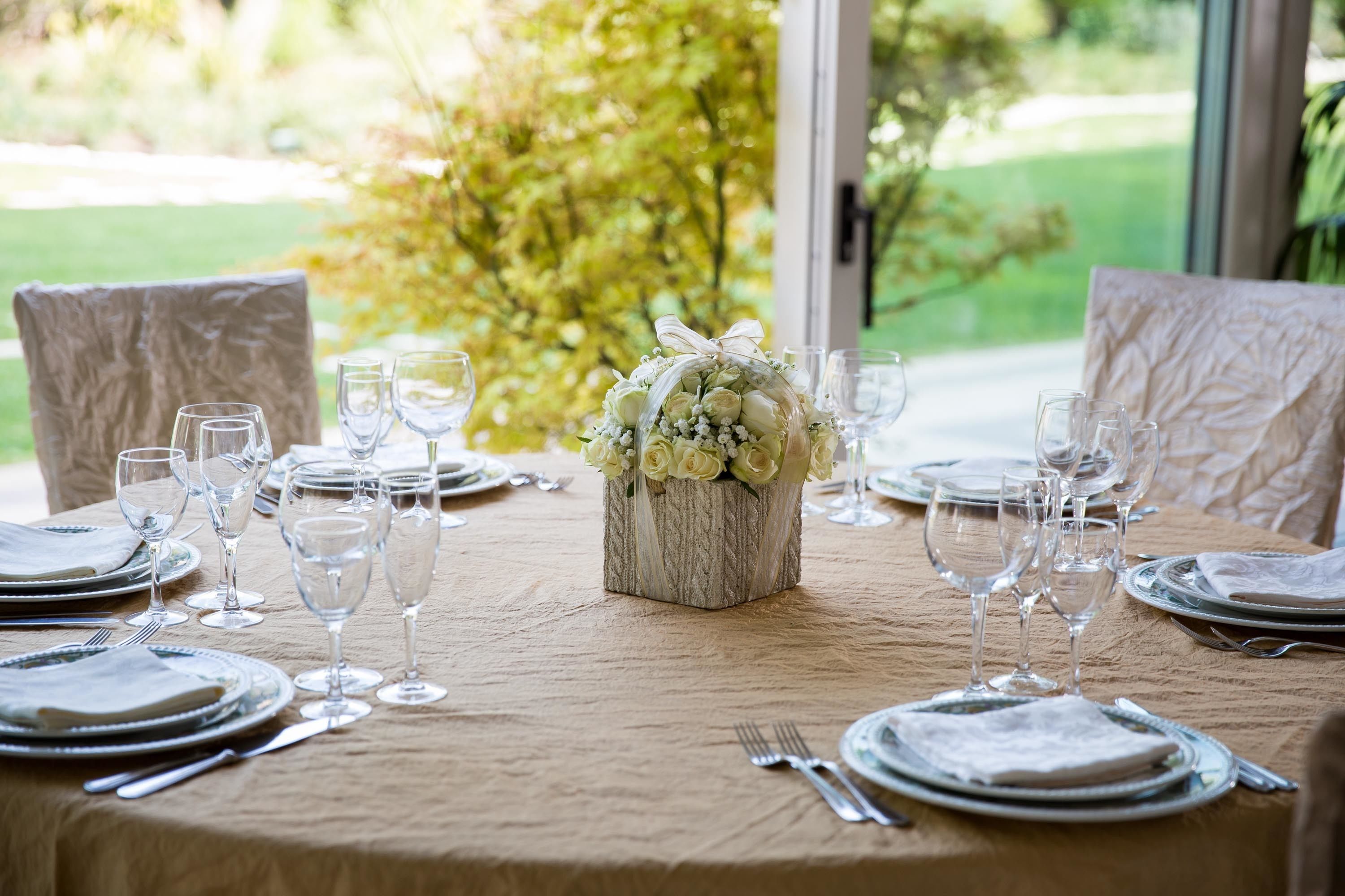 Una mesa dispuesta para una comida, con un centro de mesa floral, copas de vidrio transparente y mantel blanco.