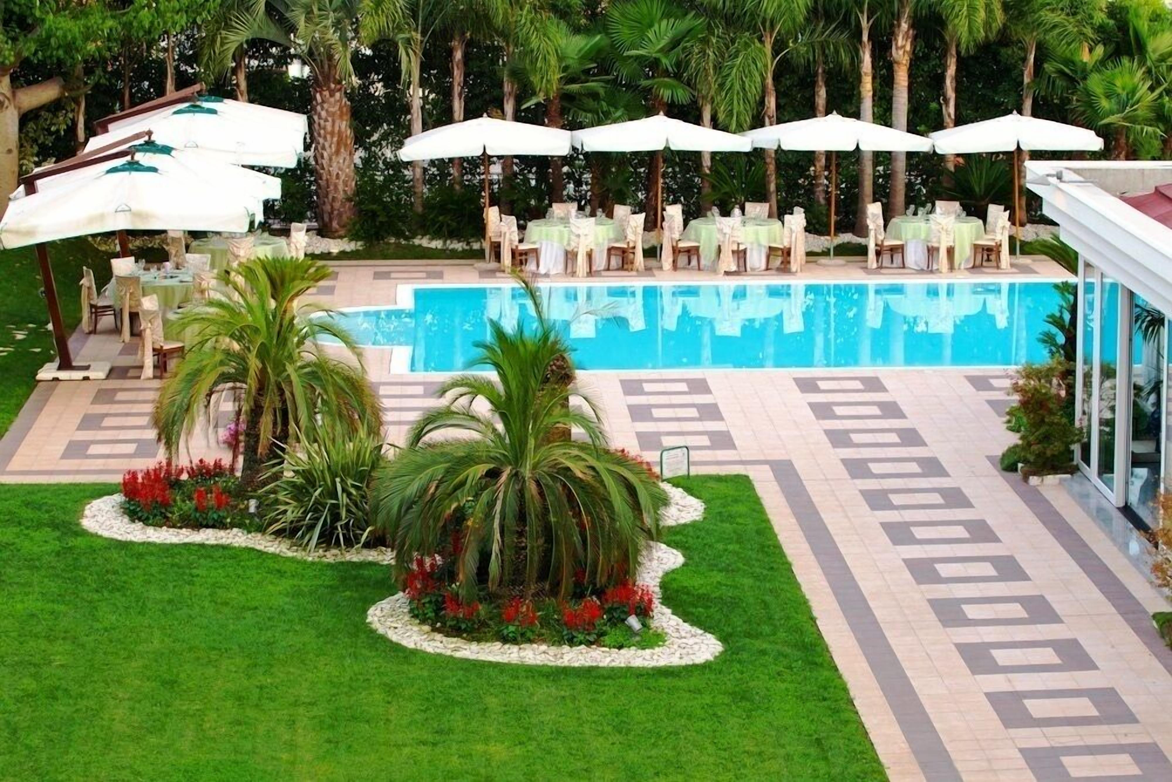 Un espace aménagé au bord de la piscine, avec des sièges extérieurs, des palmiers et une allée dallée.