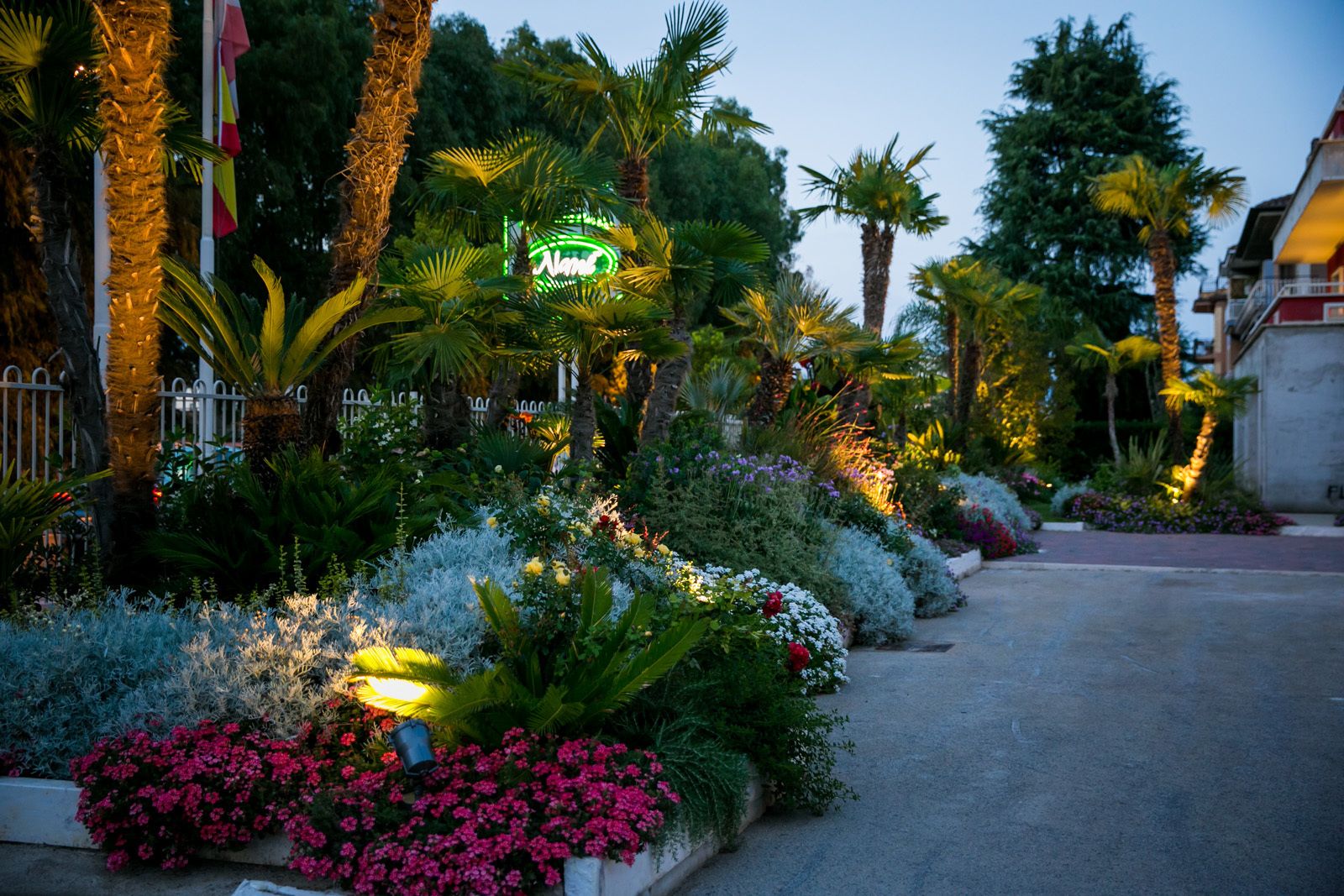Un jardín bien cuidado con diversas plantas y flores, un sendero y un letrero de neón.