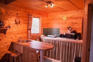 Cocina de cabaña de madera con una barra de madera, taburetes, un fregadero, un microondas y una ventana con cortinas escocesas.