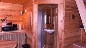 A wooden cabin interior with a kitchen area, a sink, and a door leading to another room. - Les Chalets du Trappeur avec Spa et Sauna (Wentworth-Nord)