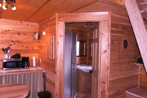 Interior de una cabaña de madera con cocina, un lavabo y una puerta que da a otra habitación.