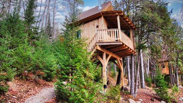 A wooden treehouse with a balcony, surrounded by dense forest and a clear sky. - Les Chalets du Trappeur avec Spa et Sauna (Wentworth-Nord)