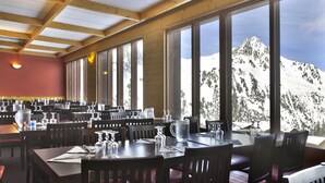 Ein Restaurant mit großen Fenstern und Blick auf die Berge. Die Tische sind mit Besteck und Gläsern gedeckt.