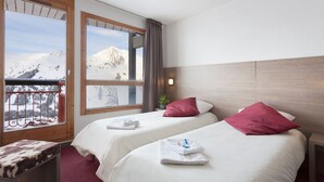 Ein Hotelzimmer mit zwei Betten, einem Balkon mit Bergblick und einem hölzernen Kopfteil.