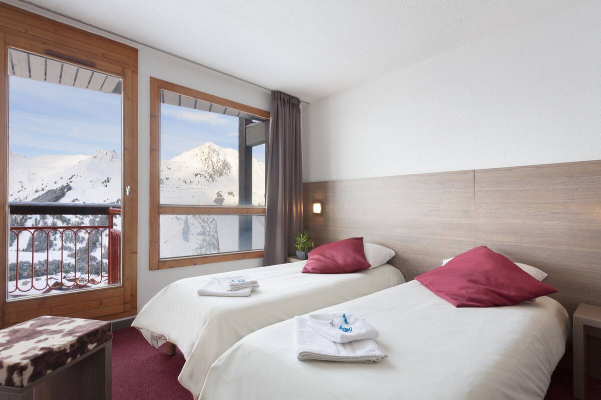 Ein Hotelzimmer mit zwei Betten, einem Balkon mit Bergblick und einem hölzernen Kopfteil.