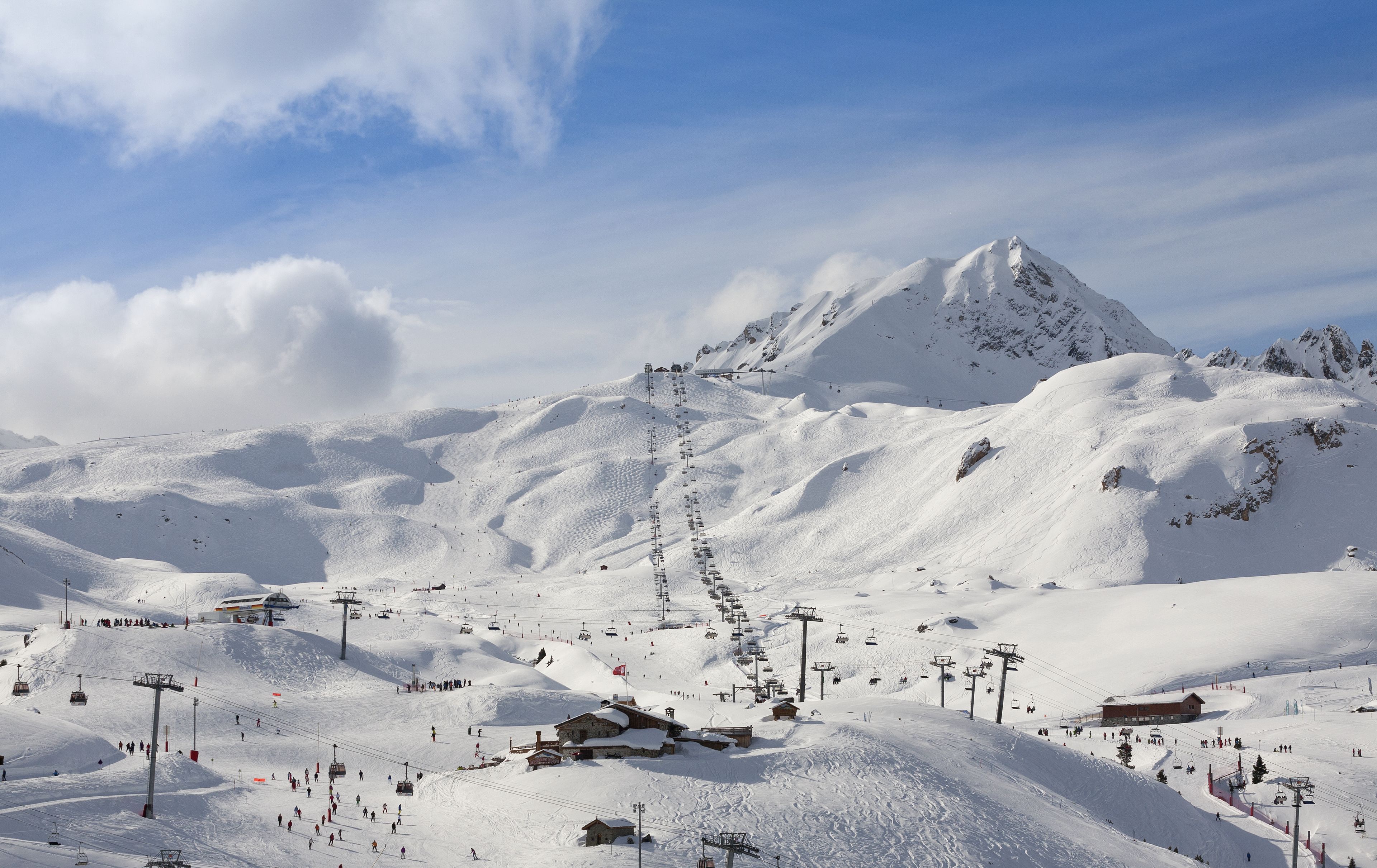 A snow-covered ski resort with ski lifts, a mountain peak, and a building.
