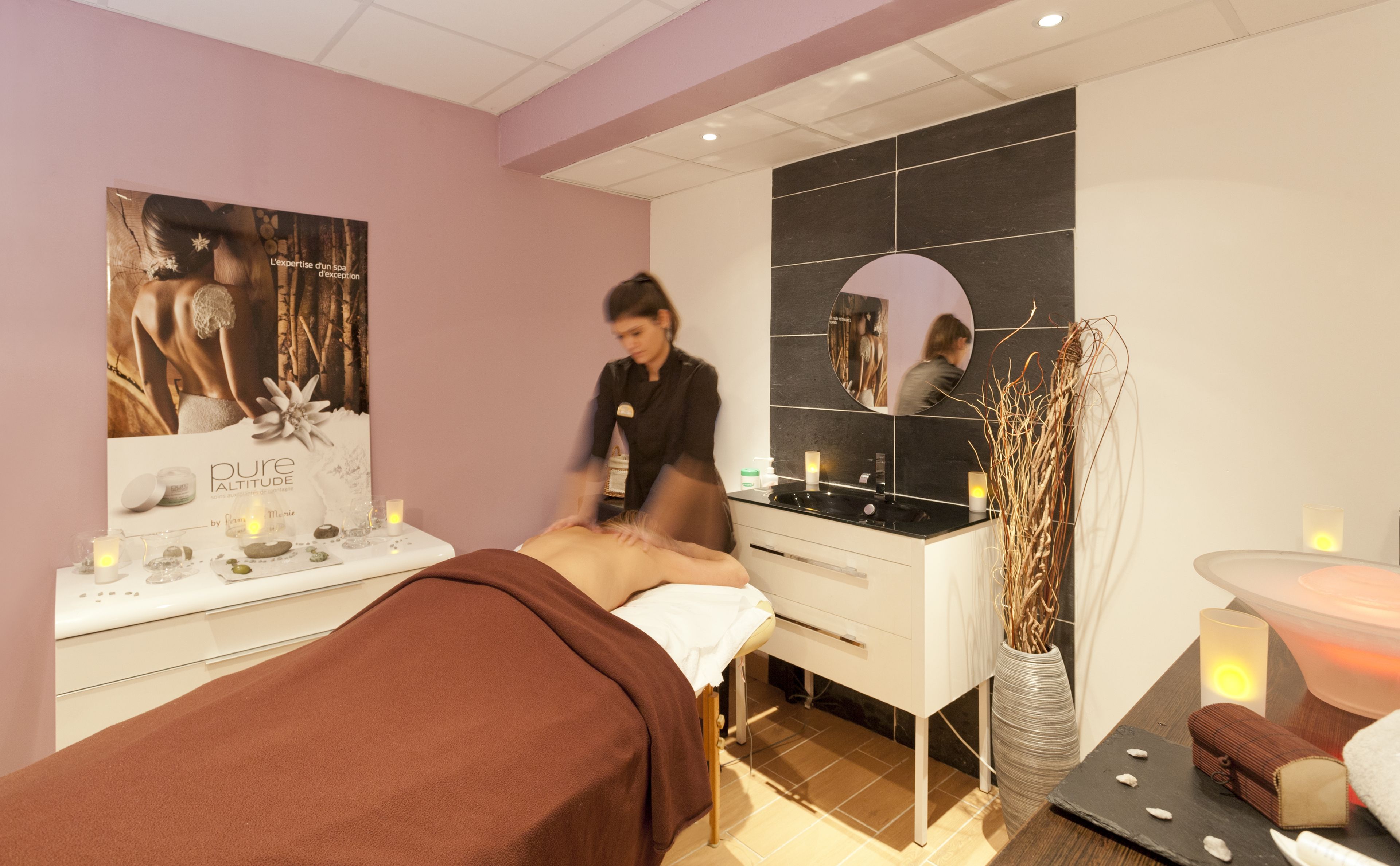 A spa room with a massage table, a mirror, a sink, and a vase with dried plants.