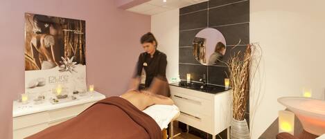 A spa room with a massage table, a mirror, a sink, and a vase with dried plants.
