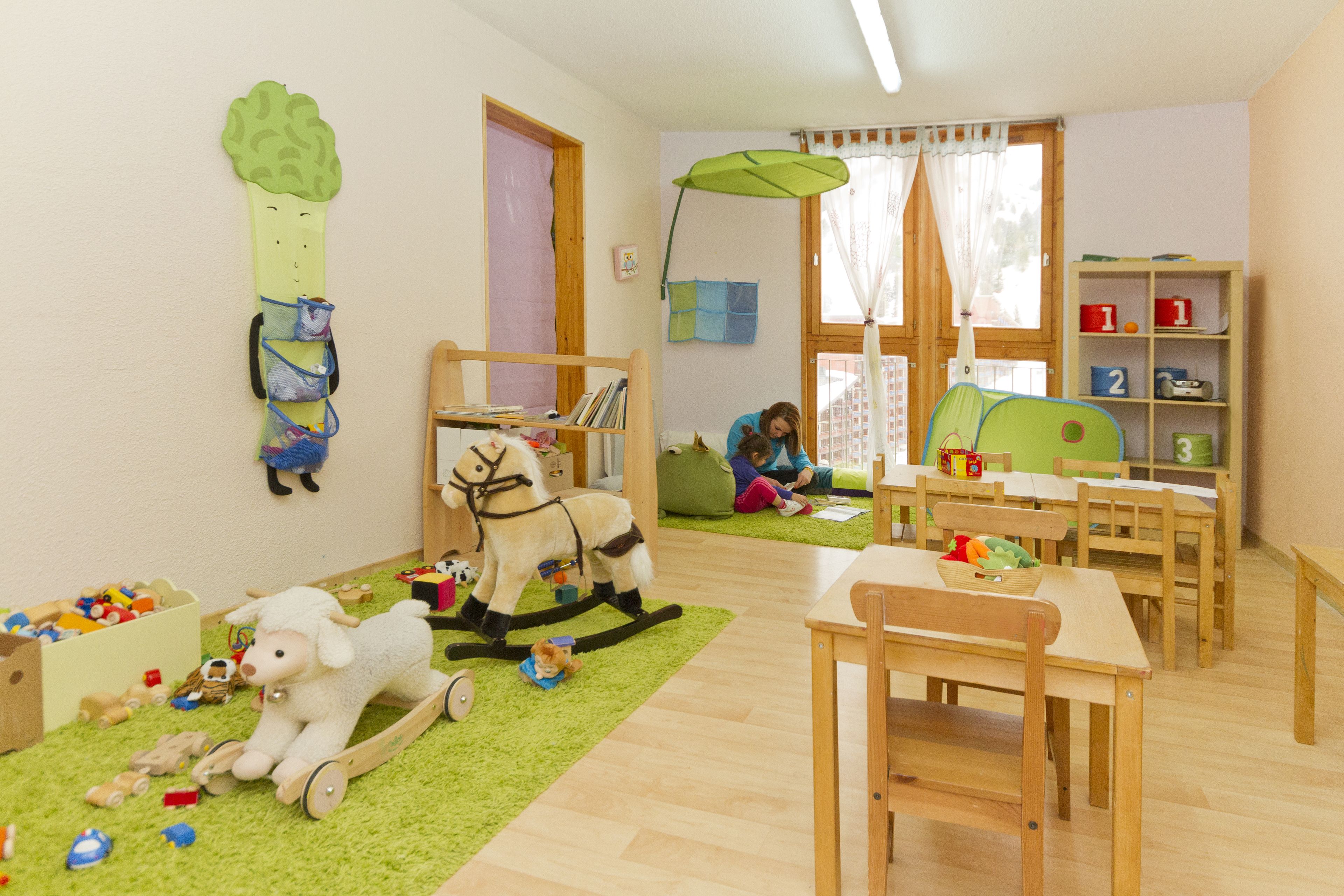 A children's playroom with wooden furniture, a rocking horse, and a green carpet.
