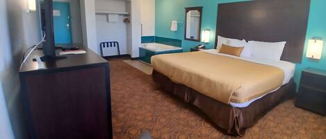 A hotel room with a bed, a desk with a computer, a bathroom, and a door.