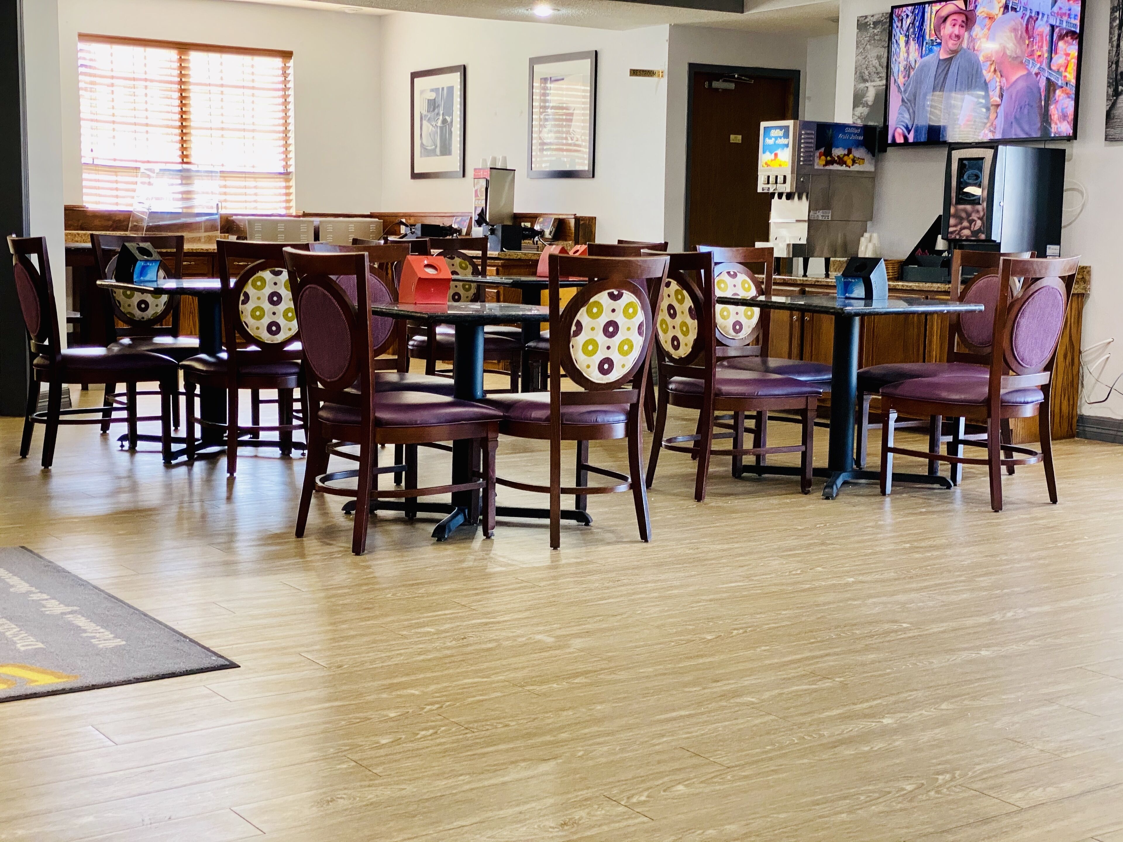 A restaurant with wooden tables and chairs, a coffee machine, and a TV screen displaying a show.
