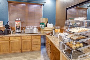 A breakfast buffet area with a waffle maker, coffee machine, and various food items.