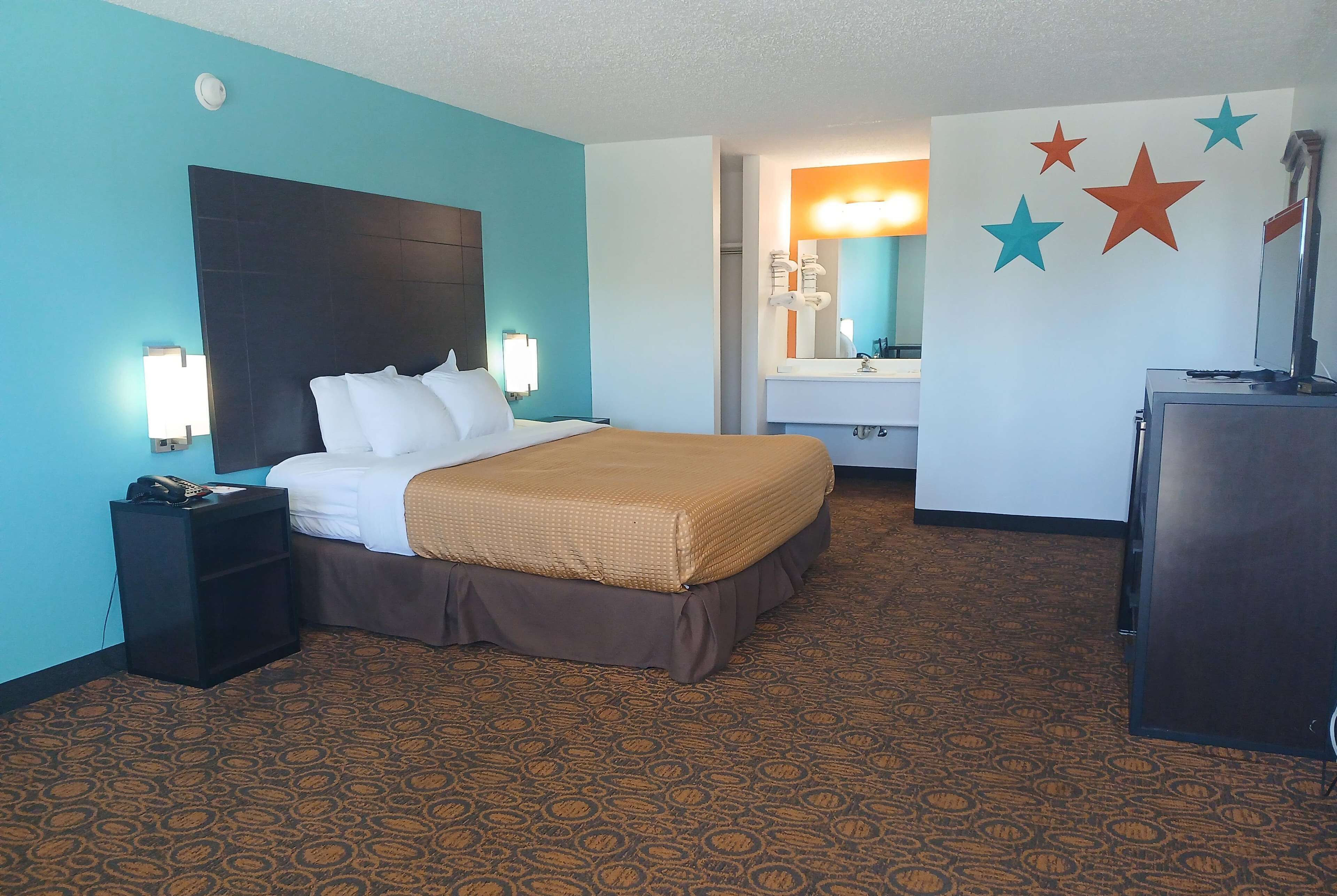 A hotel room with a bed, a nightstand, a desk, a mirror, and a wall with star decorations.