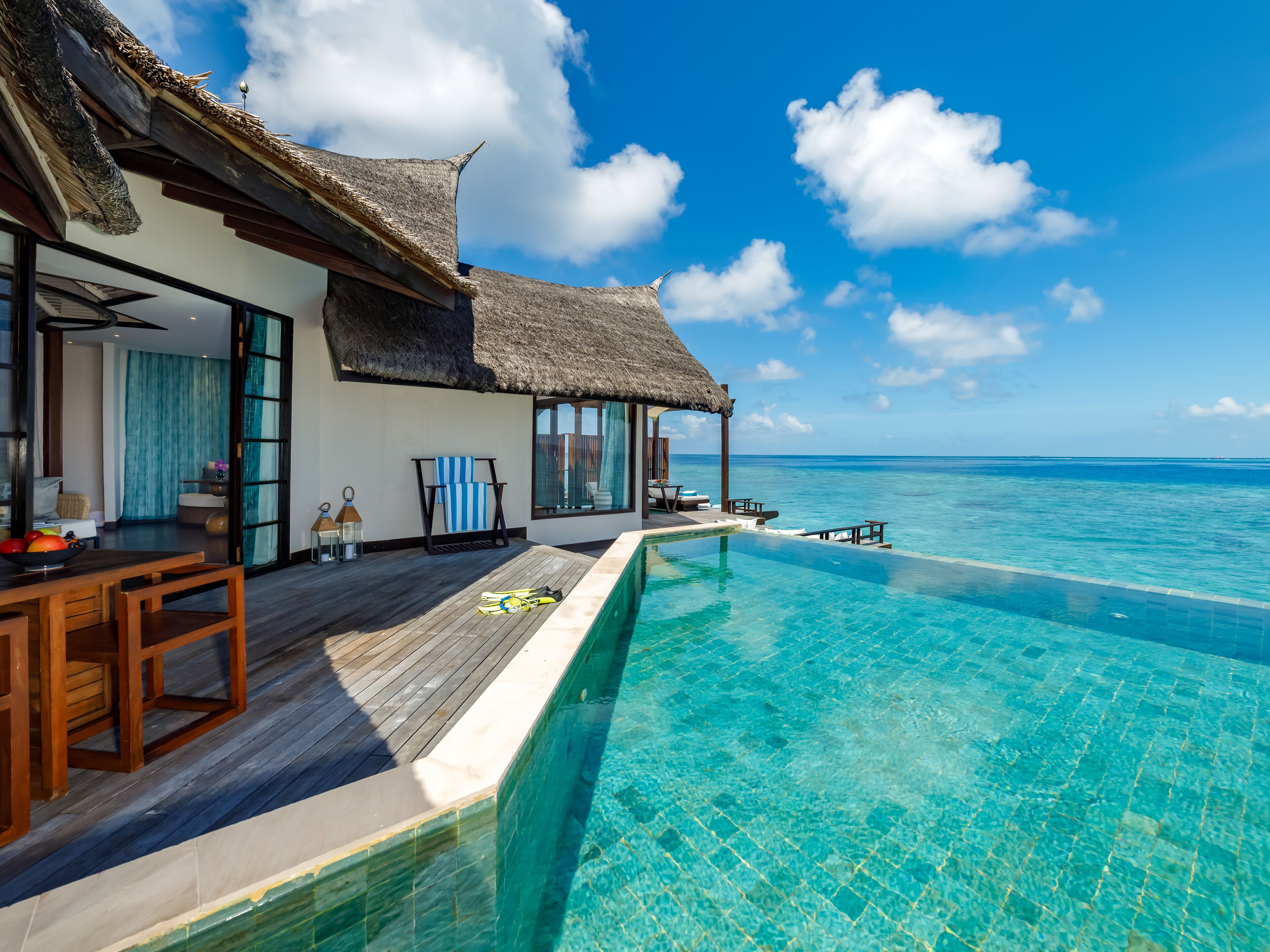 An infinity pool with a wooden deck, a thatched-roof structure, and a view of the ocean.