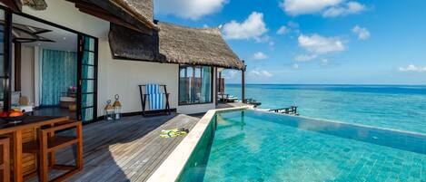 An infinity pool with a wooden deck, a thatched-roof structure, and a view of the ocean.