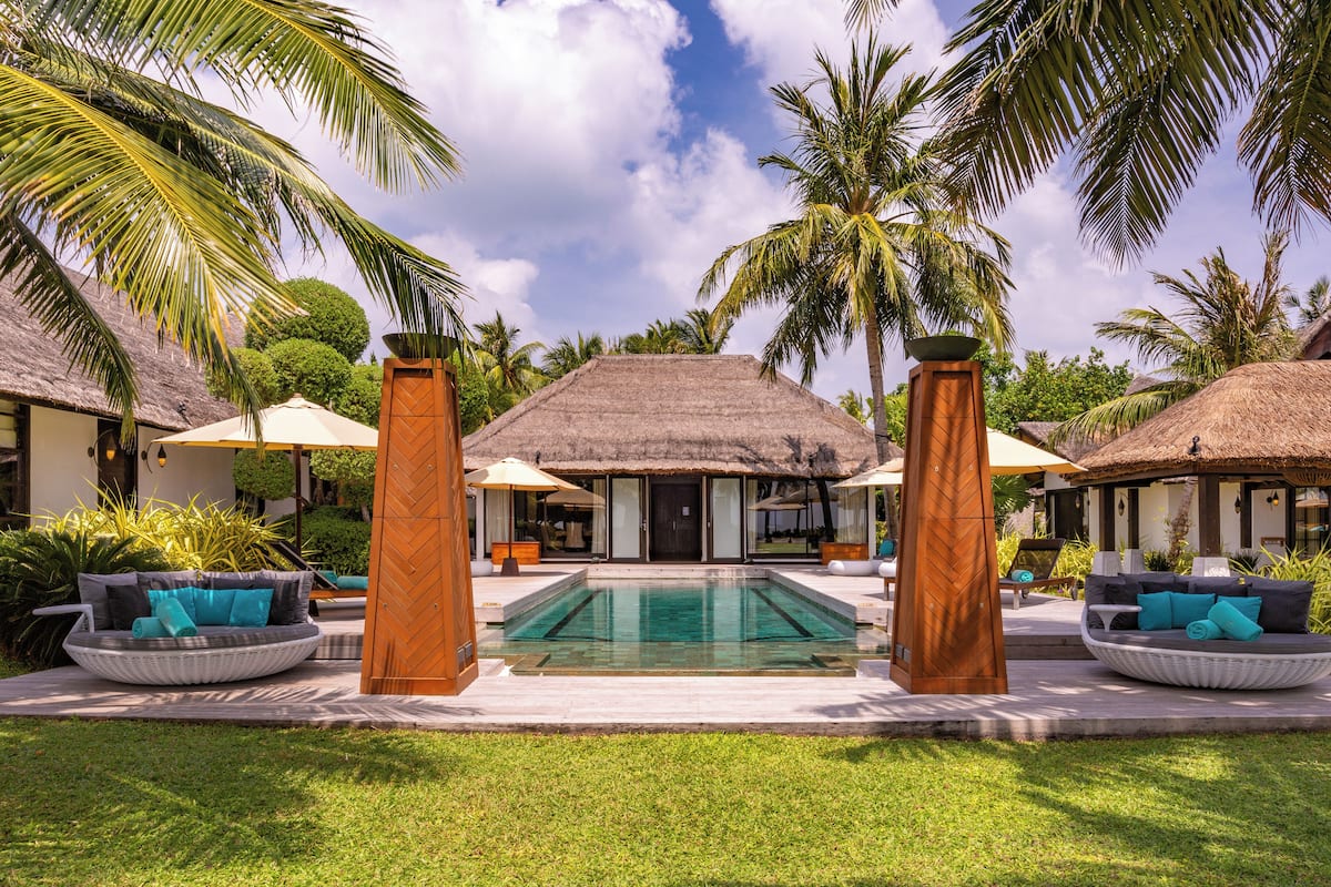 A pool area with a thatched-roof structure, lounge chairs, and palm trees.