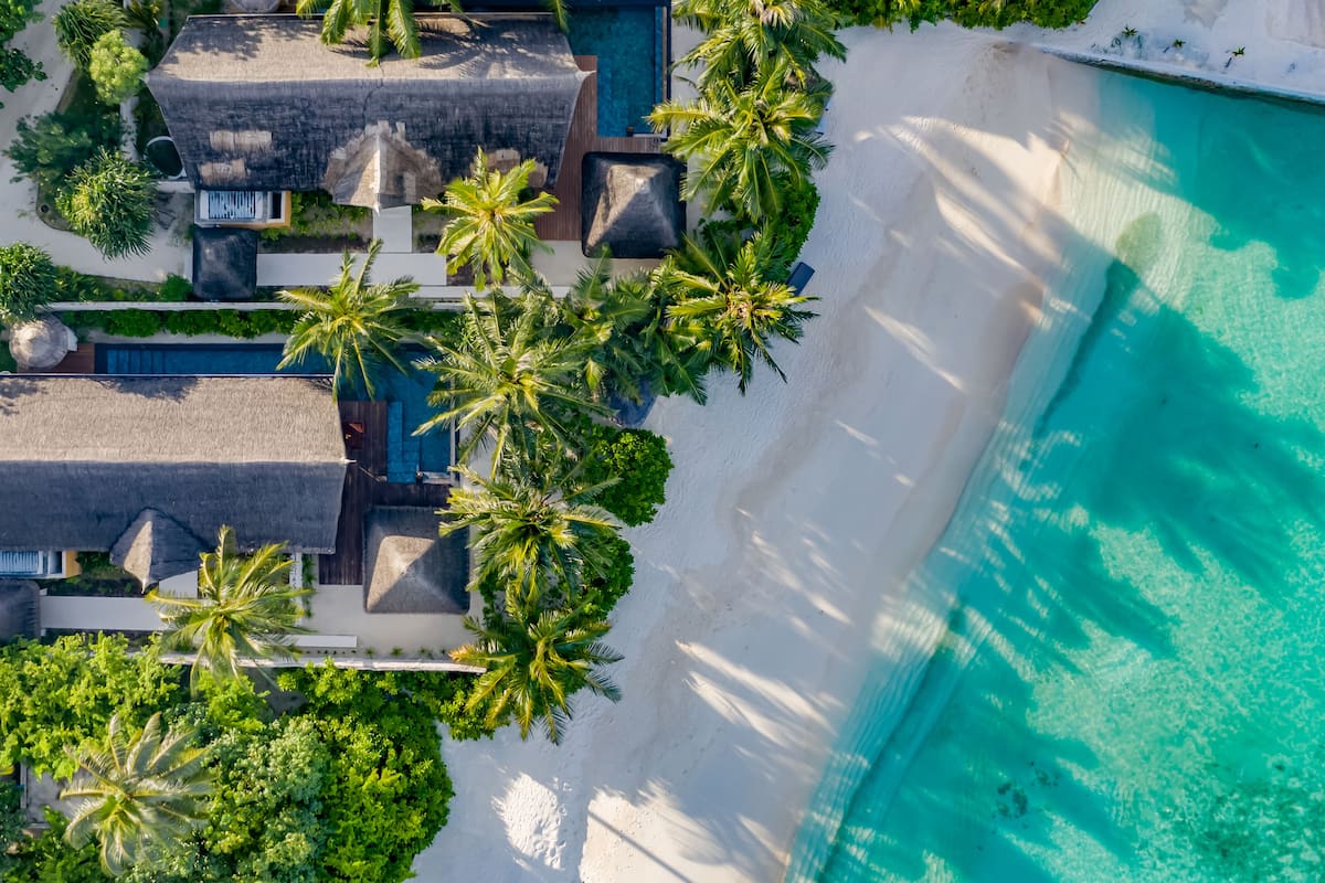 An aerial view of a resort with multiple buildings, a large swimming pool, and lush greenery.
