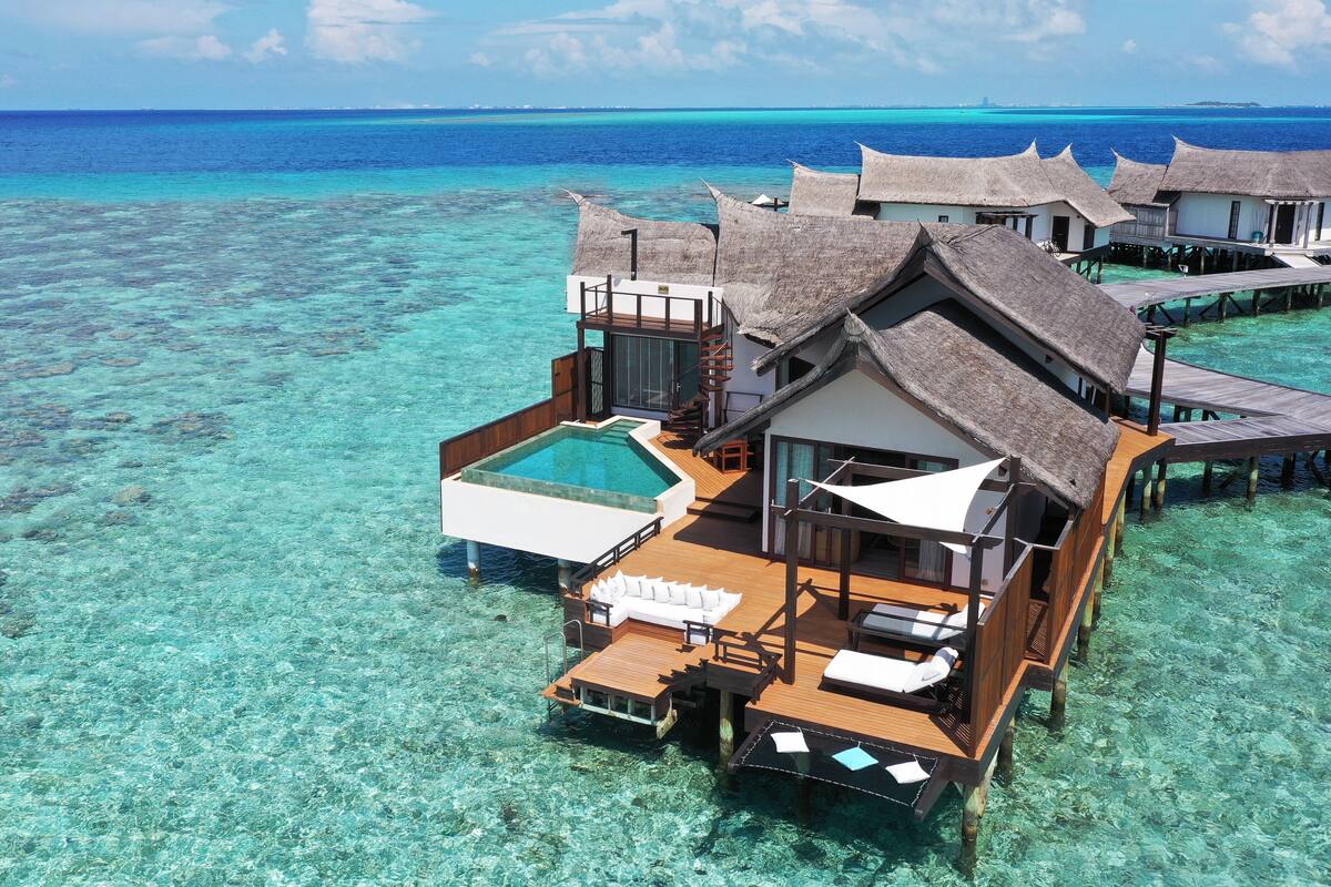 Overwater bungalows with a swimming pool, wooden deck, and thatched roofs.
