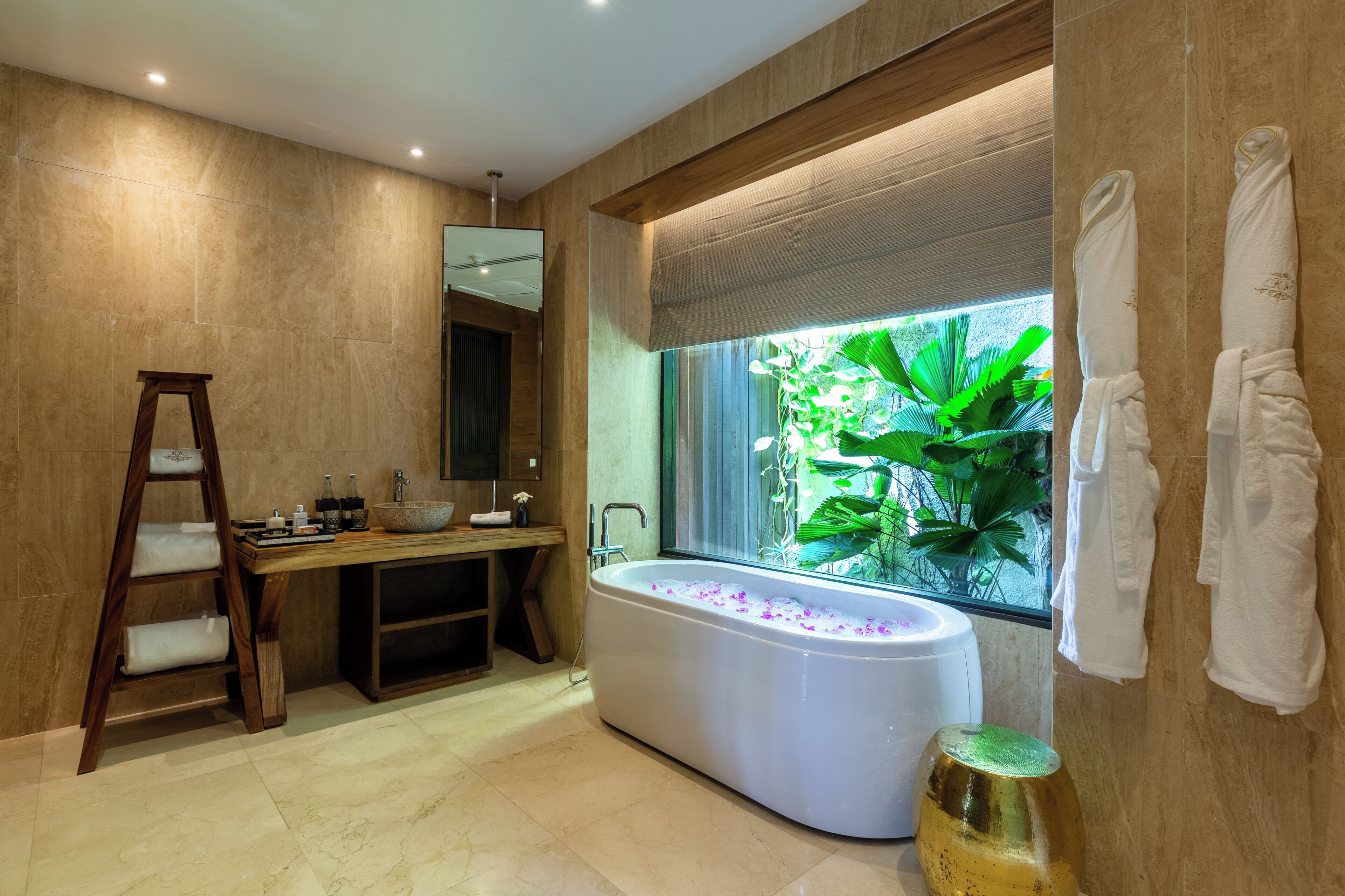 A modern bathroom with a freestanding bathtub, a wooden ladder, a large window with a view of greenery, and a vanity with a mirror and sink.
