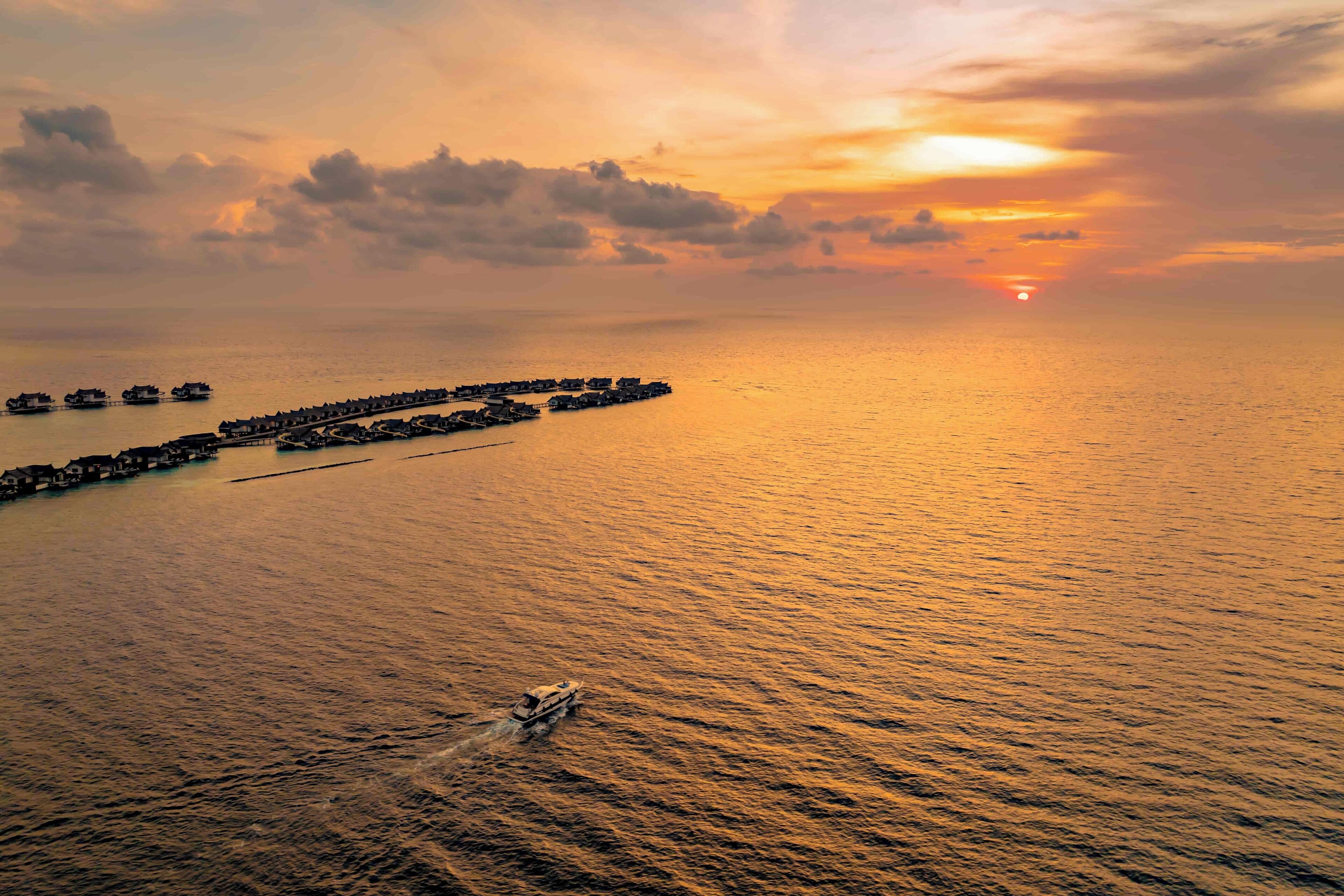 A coastal scene with a pier extending into the sea, boats docked, and a sunset in the background.