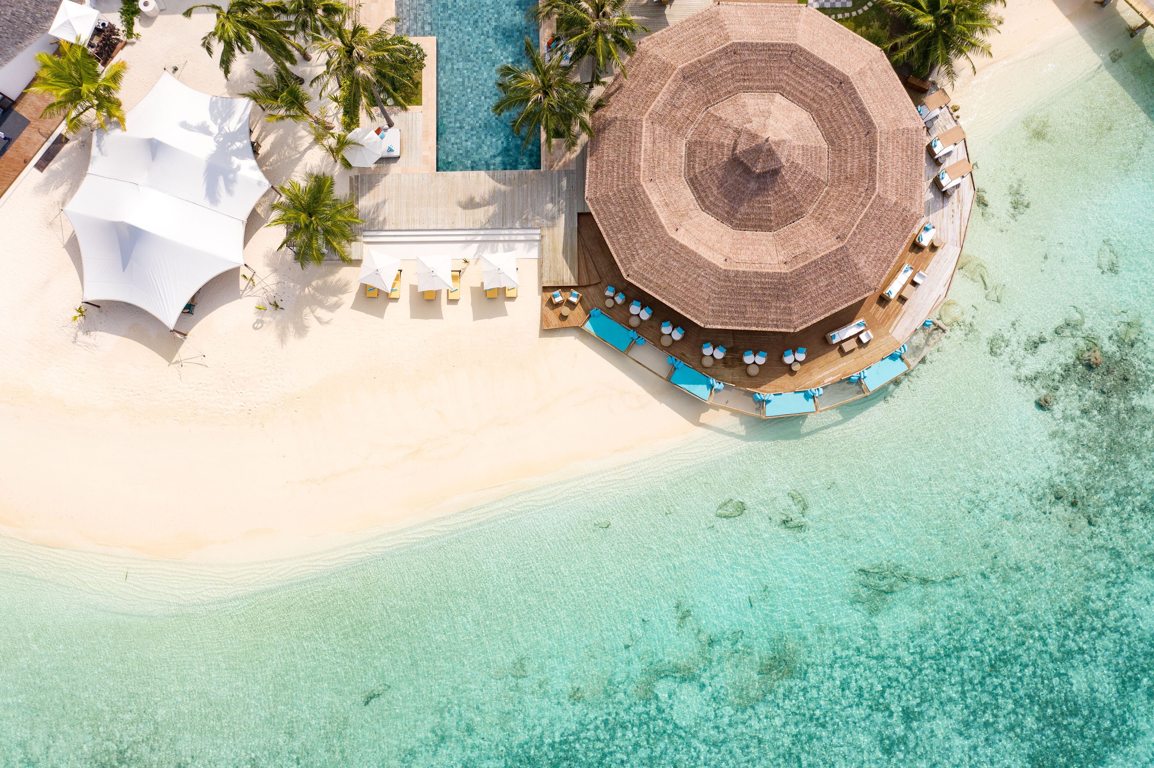 An aerial view of a resort with a pool, sun loungers, and a beach area.