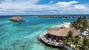 An overwater bungalow resort with thatched-roof structures connected by walkways, clear turquoise water, and palm trees. - Ozen Reserve Bolifushi- All Inclusive with Free Transfers (Bolifushi Island)