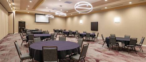 A conference room with multiple tables and chairs, a projector screen, and a carpeted floor.
