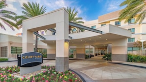 A Courtyard by Marriott hotel entrance with a covered walkway, palm trees, and a flower bed.