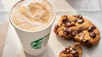 Um copo da Starbucks com uma bebida espumosa e um prato de biscoitos de chocolate.